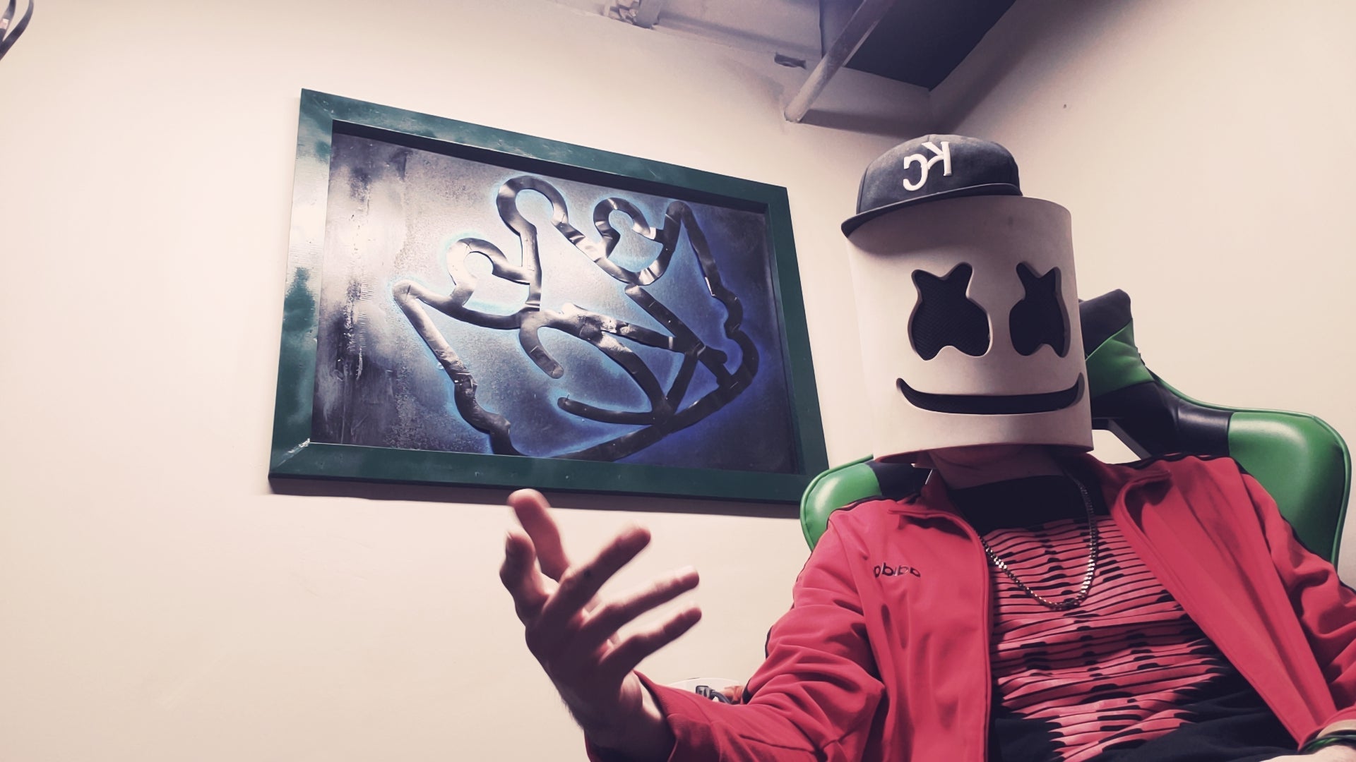 Person wearing a red jacket with a graphic design, standing next to a framed picture on a wall.